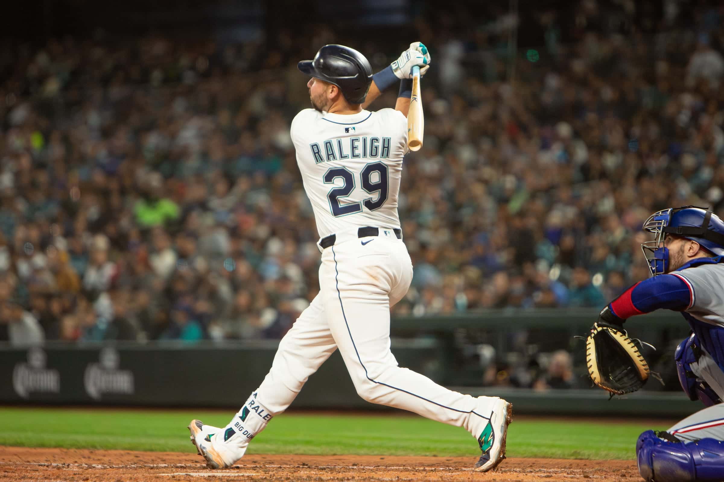 Mariners catcher Cal Raleigh, number 29, finishing a full swing at home plate under the lights