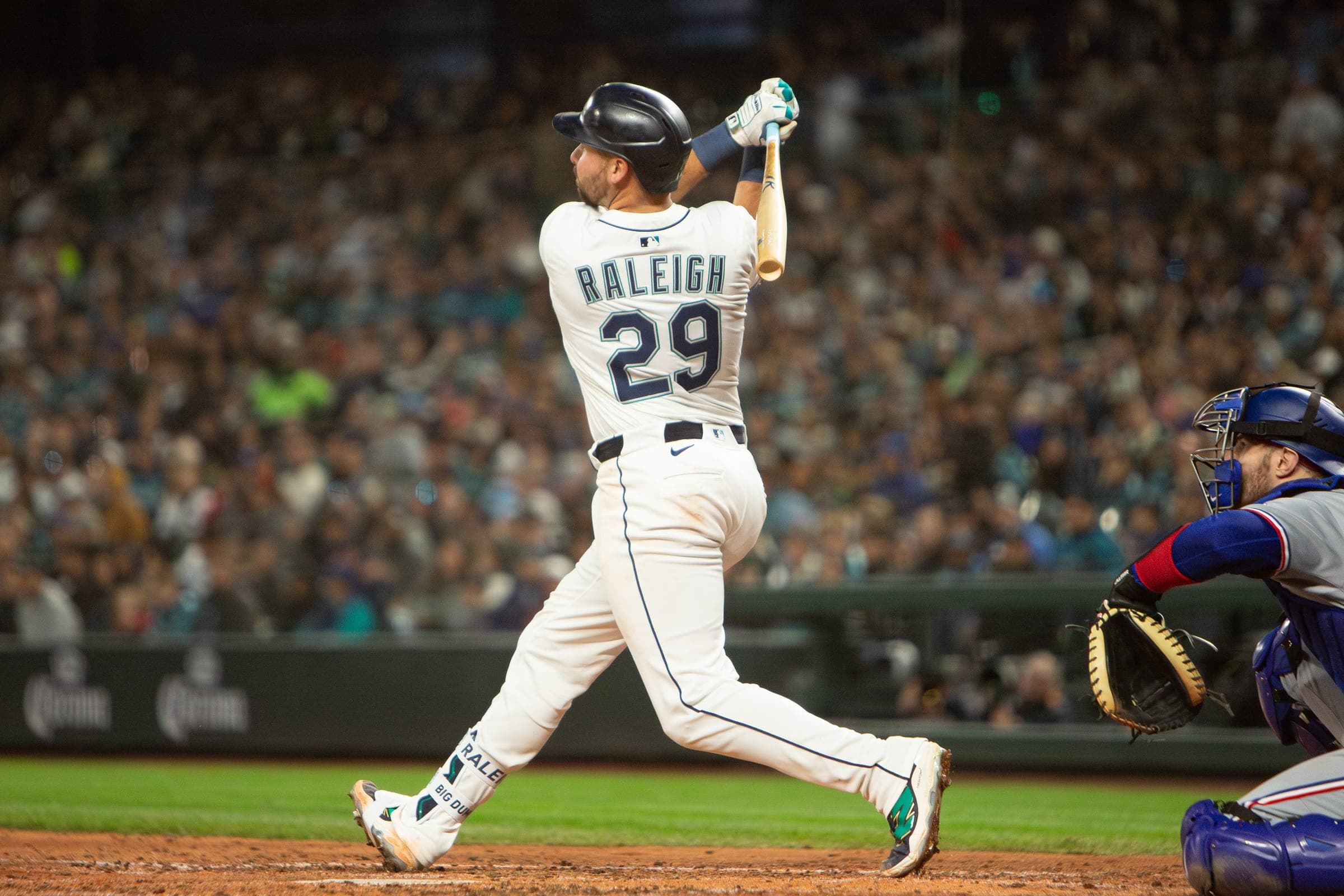 Mariners catcher Cal Raleigh, number 29, finishing a full swing at home plate under the lights