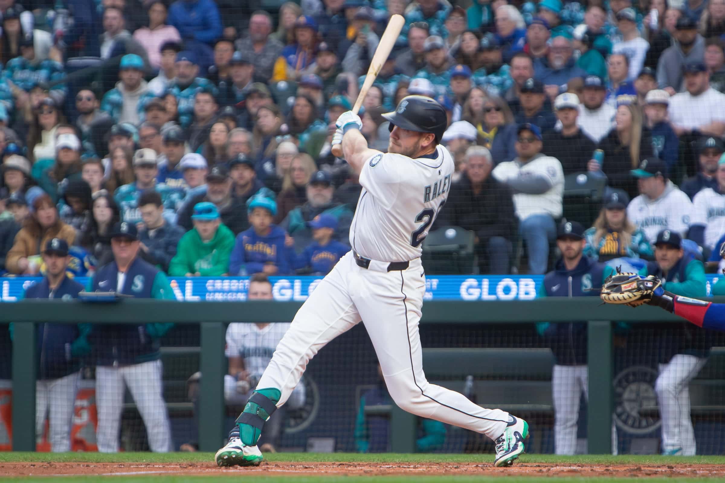 Mariners hitter at the end of his swing in front of a packed crowd behind the dugout