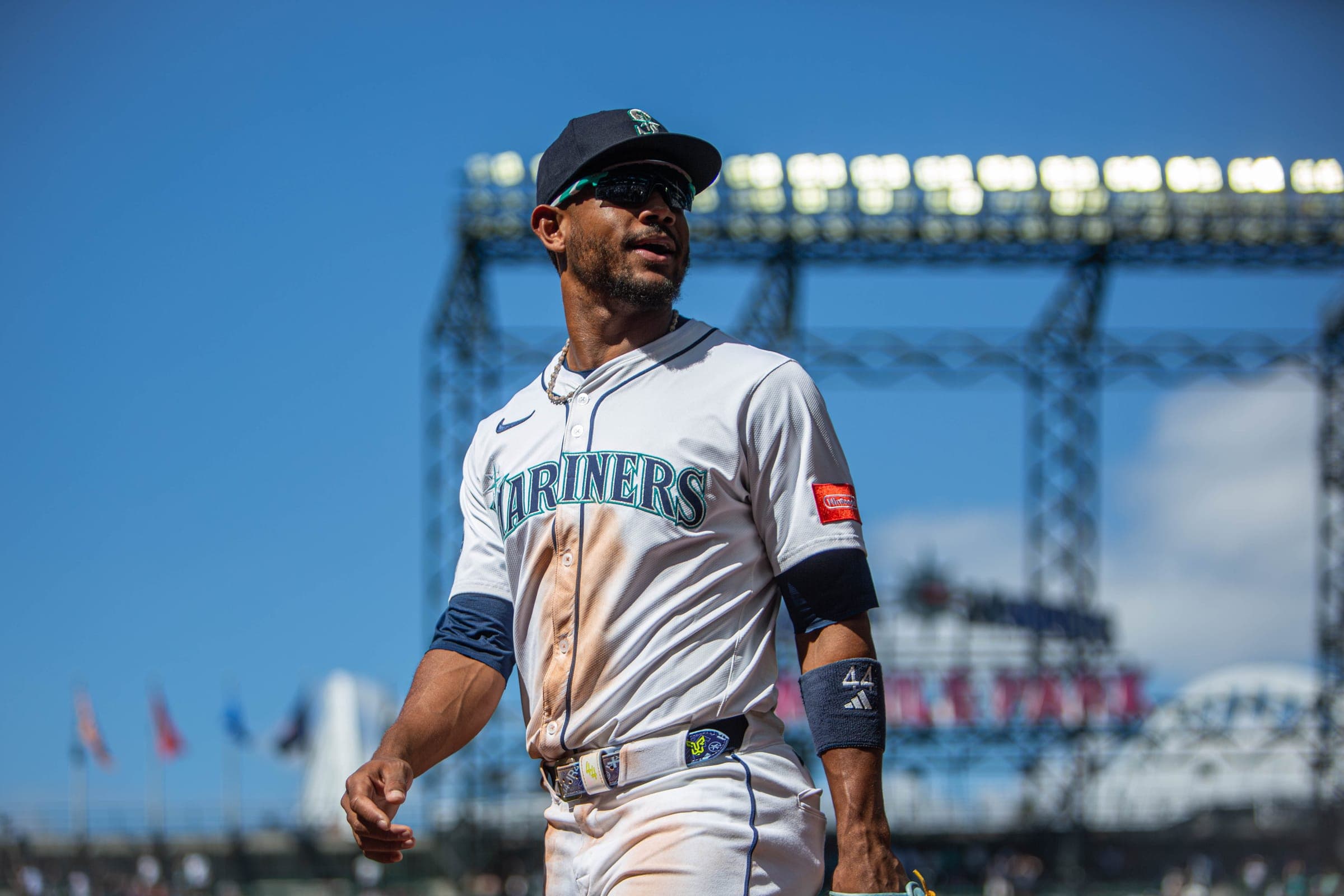 Mariners outfielder Julio Rodriguez, 44 on his wristband, walking off the field in sunglasses with dirt down his jersey