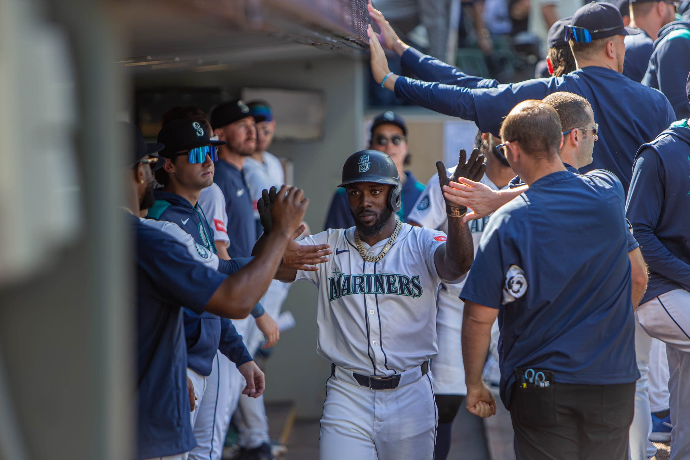 Mariners hitter in a batting helmet slapping hands with teammates and staff in the dugout