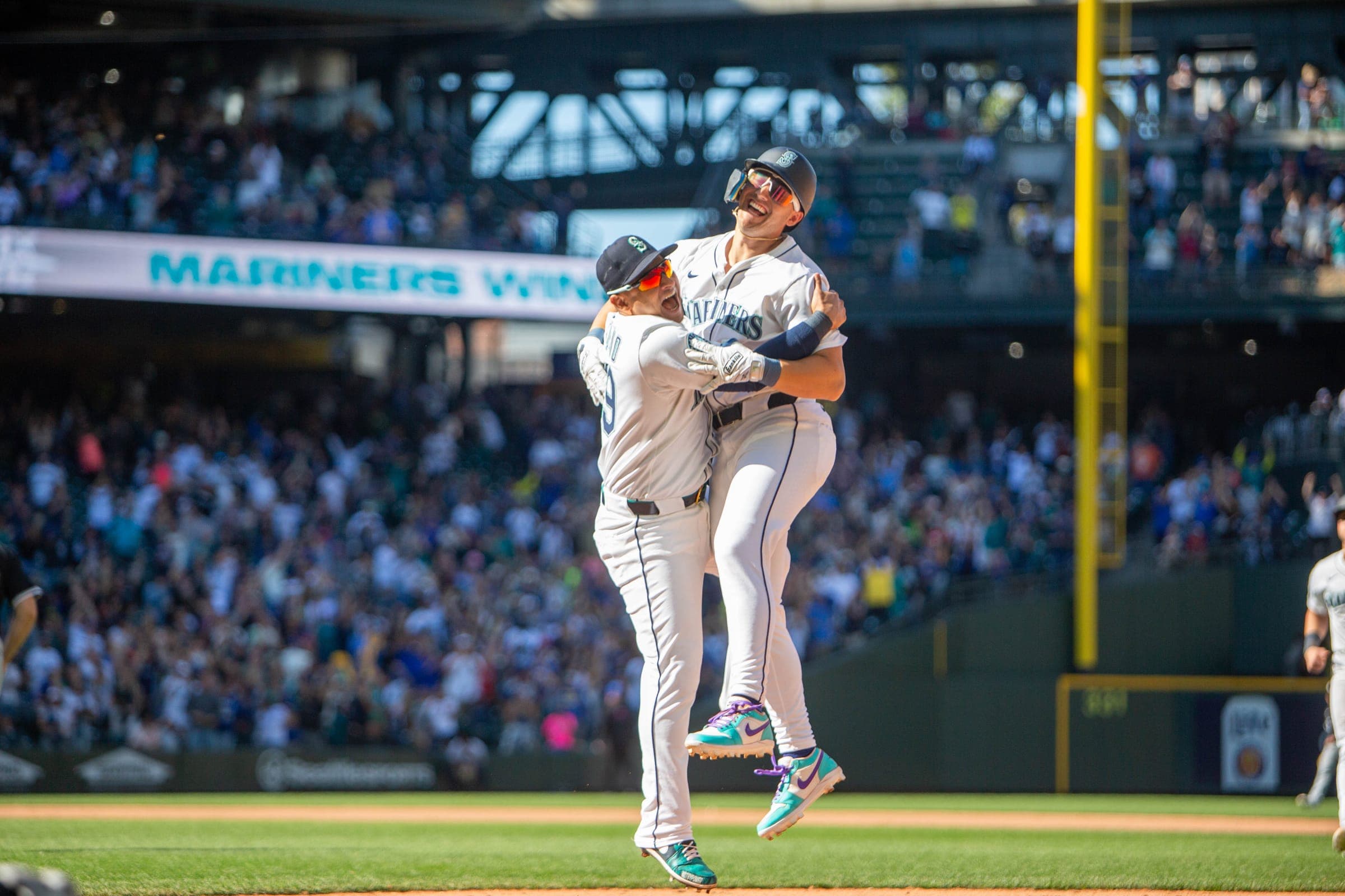 Two Mariners crashing into a jumping hug under the MARINERS WIN banner as the crowd cheers
