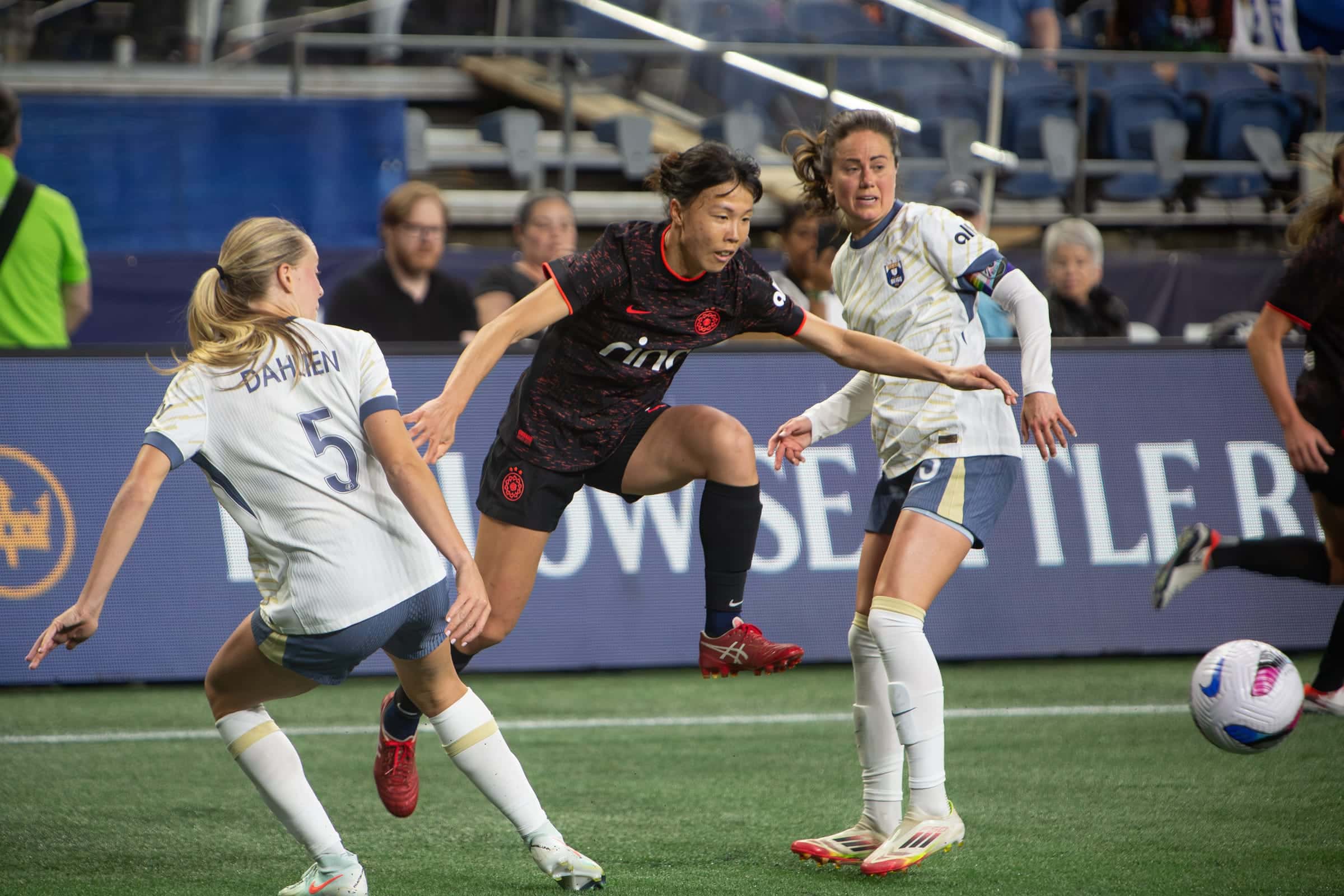 Three players converging on a loose ball in front of the Reign sideline boards