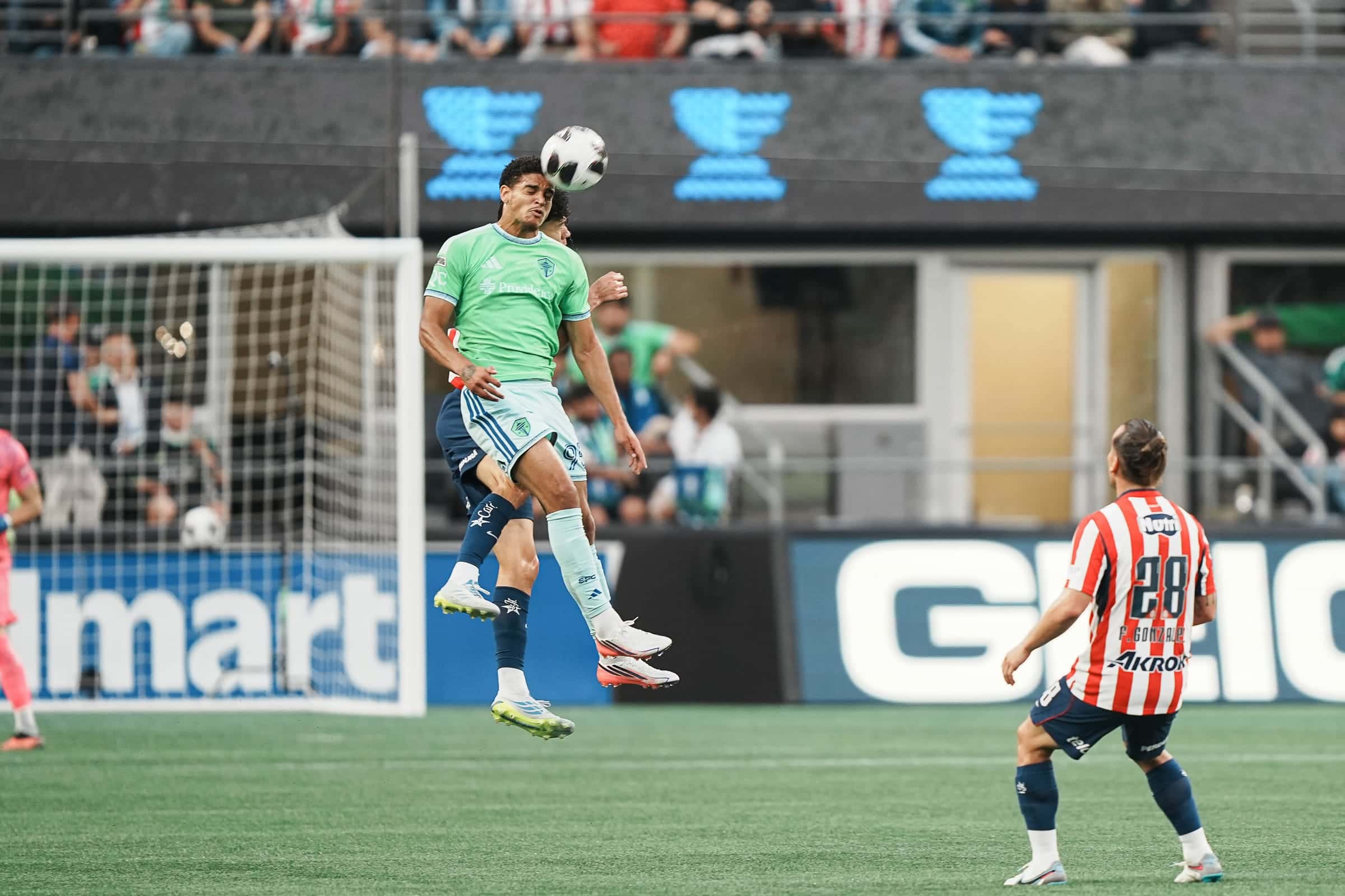 Sounders player rising high for a header in front of the goal as a Chivas player watches