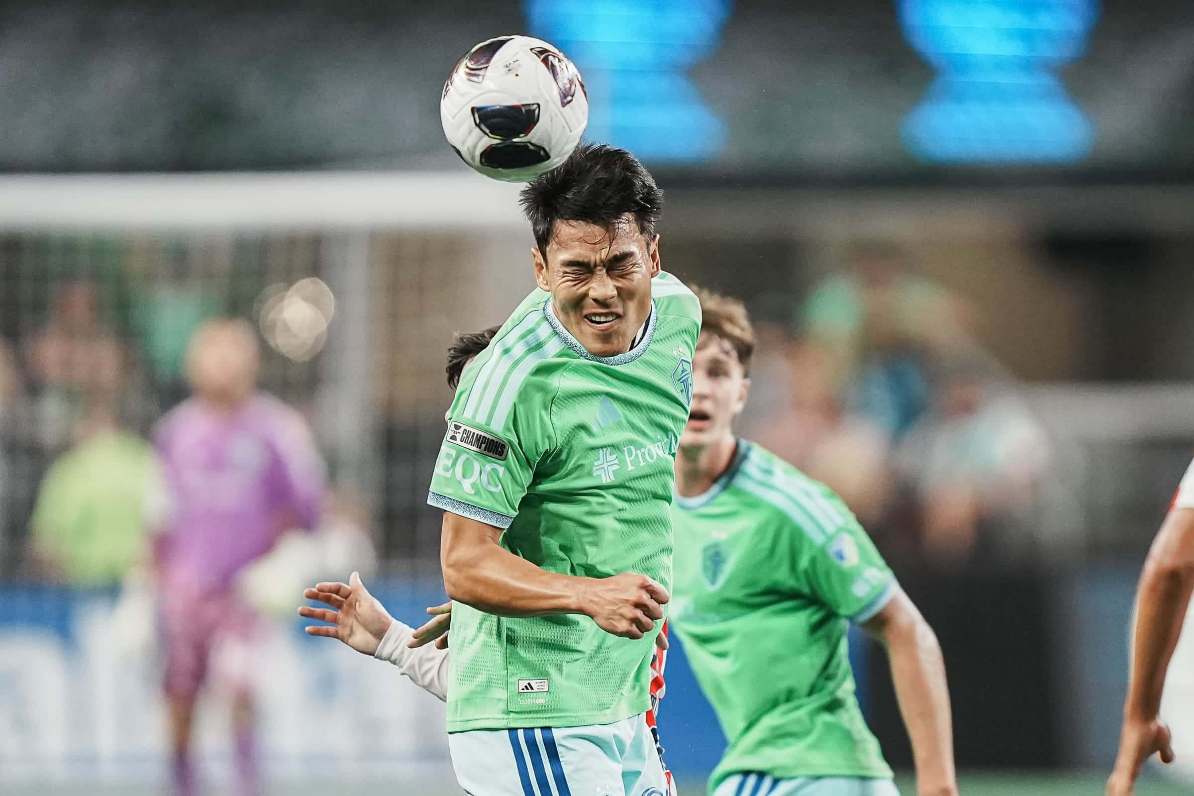 Sounders player heading the ball in a crowded penalty area