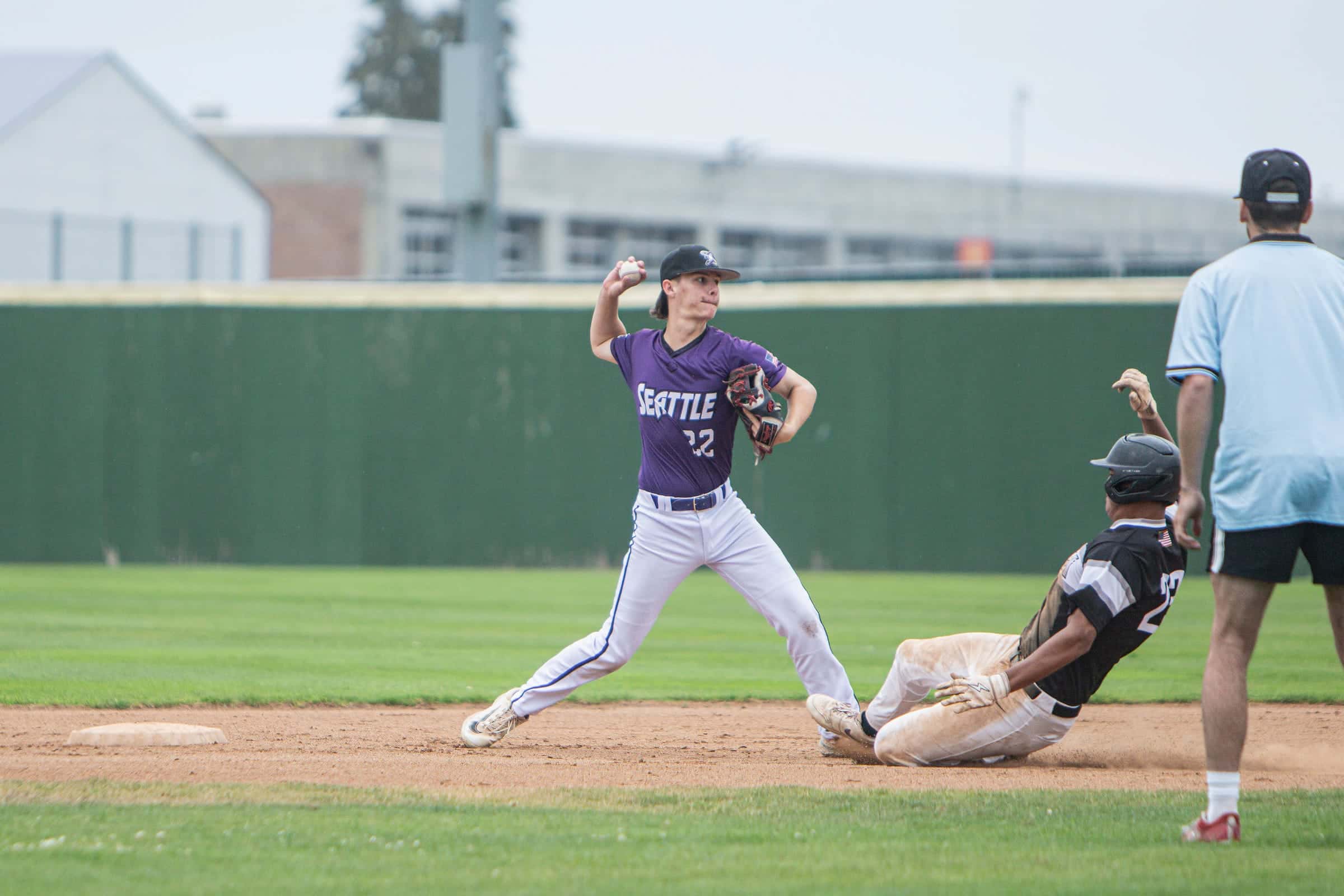Middle infielder firing to first as a runner slides into second base