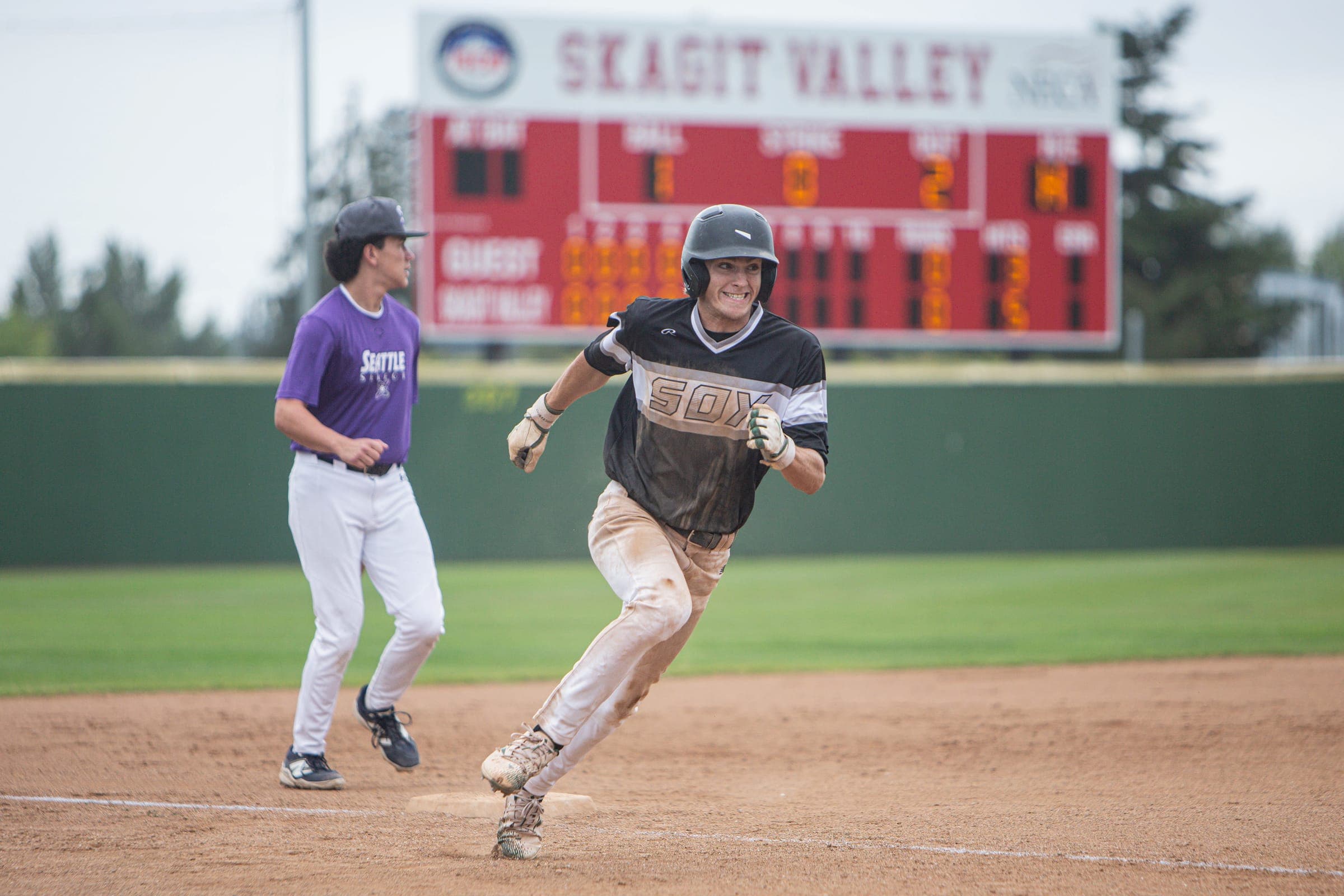 Runner charging for home with the Skagit Valley scoreboard behind him