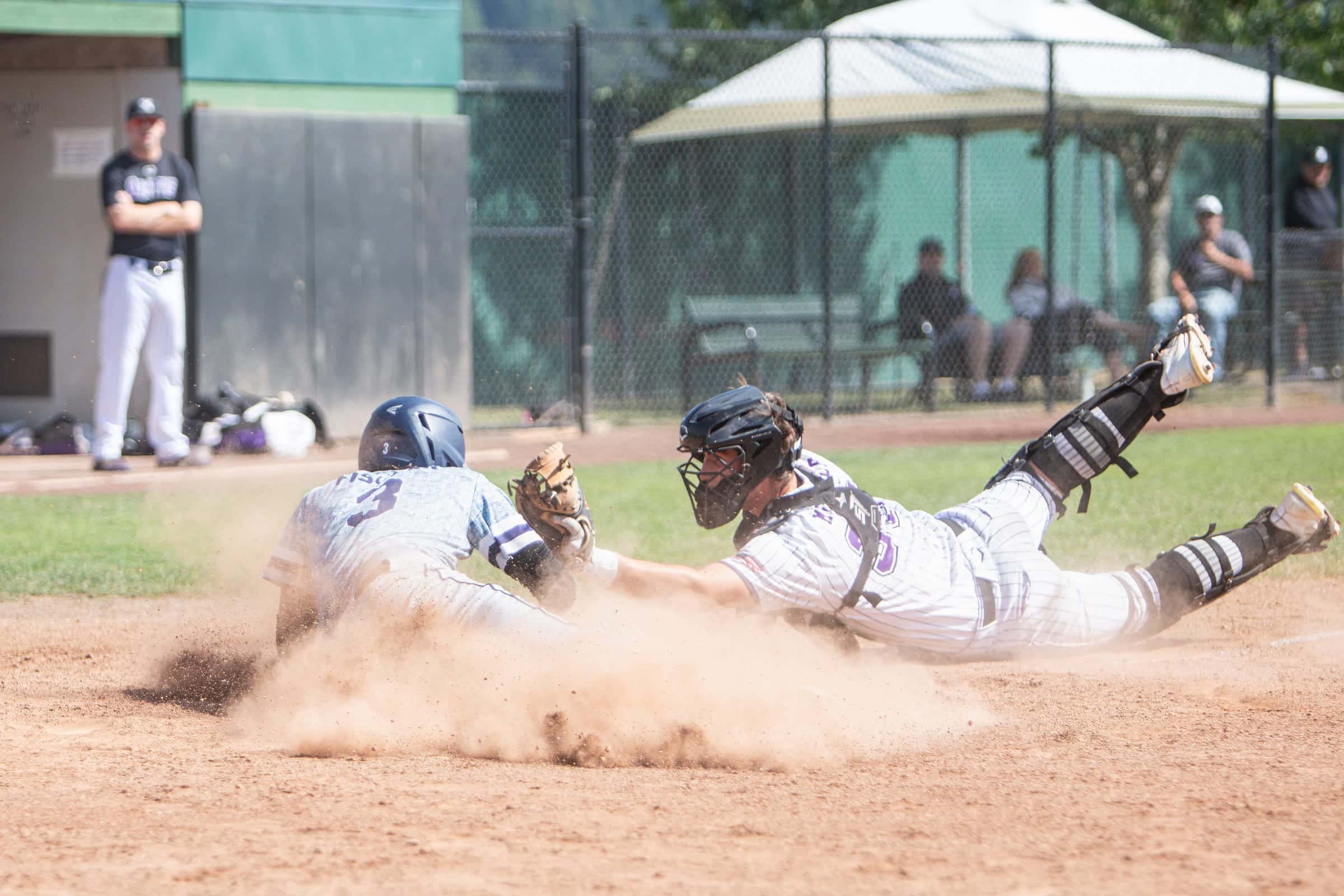 Catcher diving to tag a runner sliding into home in a cloud of dirt
