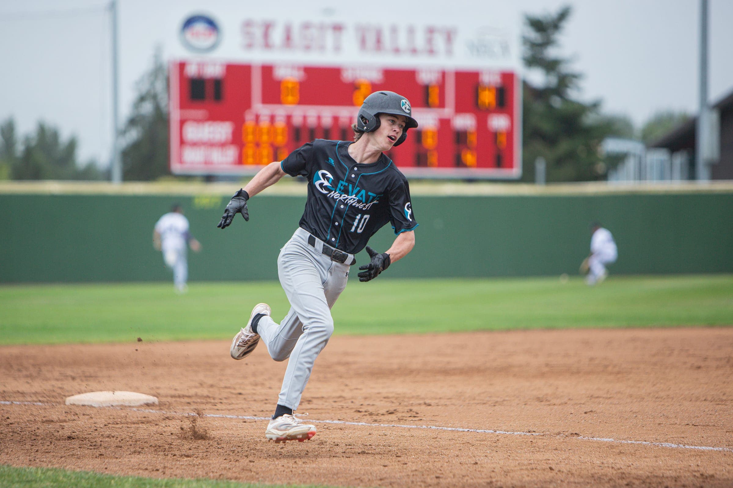 Runner in black sprinting past the Skagit Valley scoreboard