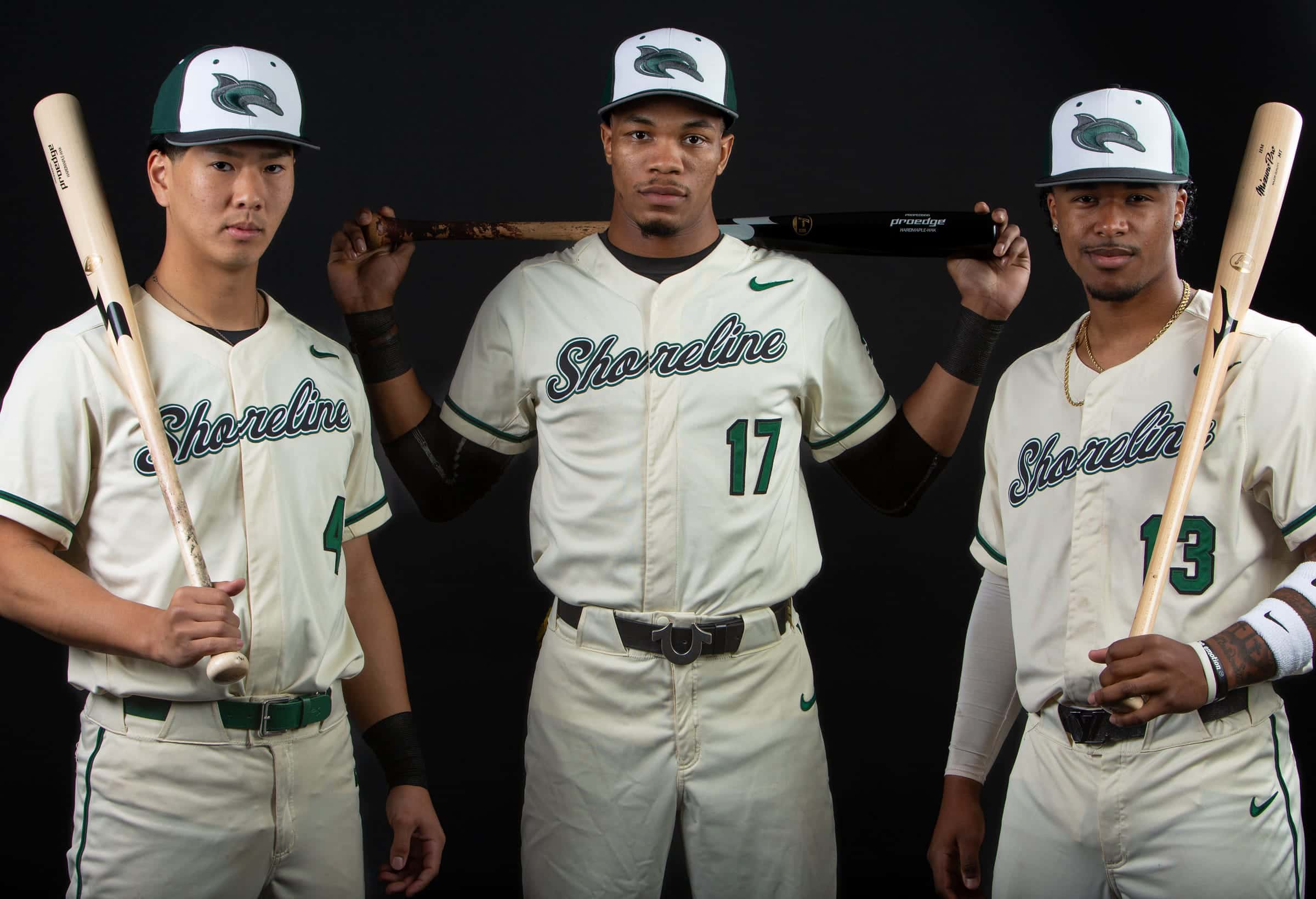 Three Shoreline players with bats posing together on a black backdrop