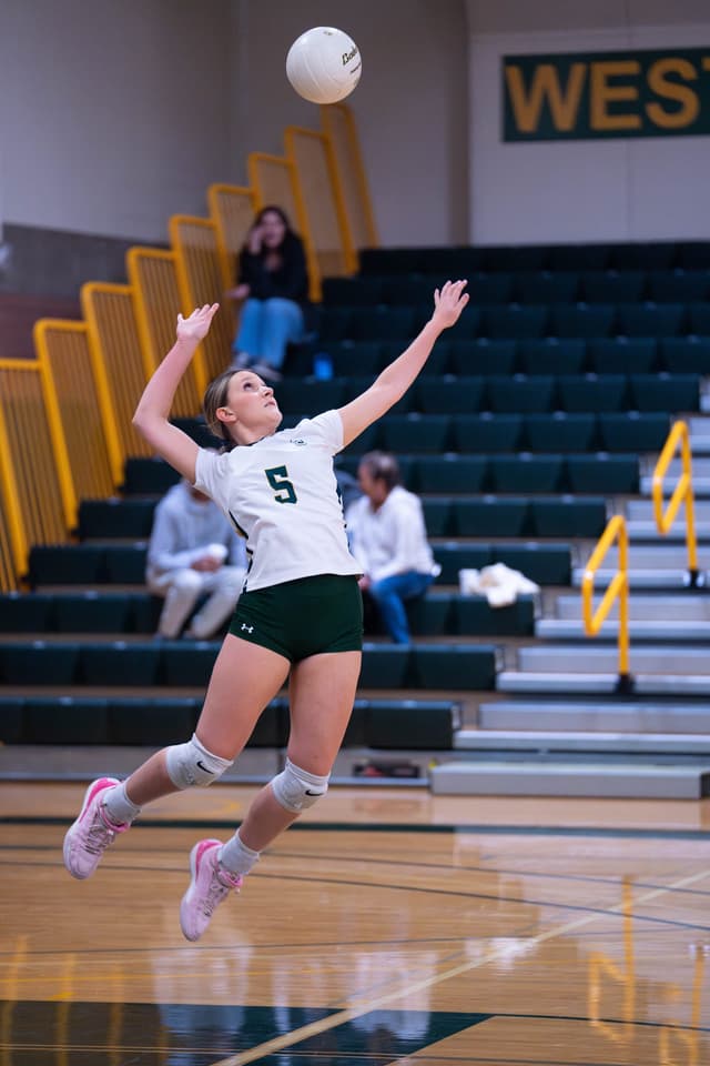 Shoreline volleyball player, number 5, rising into a jump serve